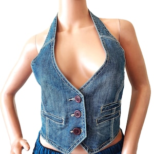 May include: A blue denim halter vest with a V-neckline and three dark purple buttons. The vest has two small pockets and white stitching details. The garment is displayed on a mannequin.