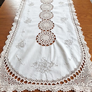 Könnte beinhalten: Weißer gehäkelter Tischläufer mit einem zarten Blumendesign und einem Mittelstreifen aus gehäkelten Kreisen.