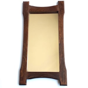Könnte beinhalten: Rechteckiger Spiegel mit einem dunkelbraunen Holzrahmen. Der Rahmen hat ein einzigartiges, geschwungenes Design an der Ober- und Unterseite, und der Spiegel selbst hat einen goldenen Farbton. Der Spiegel ist vor einem weißen Hintergrund platziert.