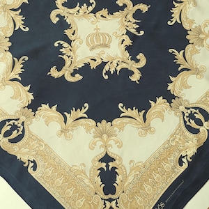 Puede incluir: Un pañuelo cuadrado con un diseño barroco en azul marino, crema y dorado. El pañuelo presenta un motivo de corona central y adornos ornamentados. El borde tiene un patrón de cachemira repetido. El pañuelo es probablemente de seda.