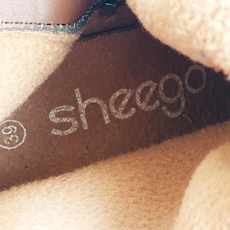 May include: Close-up of the inside of a shoe, displaying the brand name "sheego" in a light colour. The number "39" is visible on the left. The shoe's interior is a light brown colour.