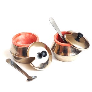 Peut inclure: Deux bols à condiments métalliques avec des extérieurs argentés brillants et des intérieurs marbrés de couleur corail vif. Chaque bol comprend un couvercle amovible assorti avec un petit bouton noir et une fine cuillère en métal argenté.
