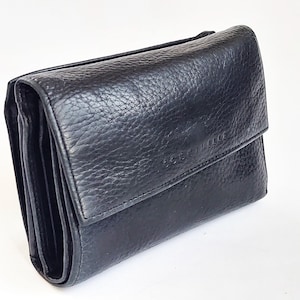 May include: A black leather wallet with a textured surface. The wallet has a fold-over flap closure and multiple compartments. The brand name "COCCINELLE" is subtly embossed on the front. The wallet is designed to hold cards, cash, and other essentials.