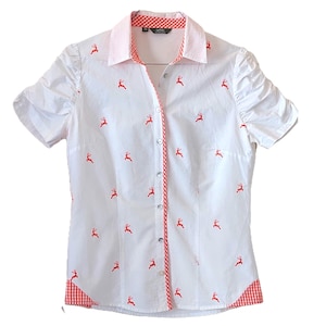 May include: White short-sleeved shirt with a light pink collar and red gingham trim. The shirt features a pattern of small red deer. The buttons are silver. The shirt is on a hanger.