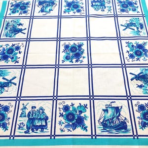May include: A white tablecloth with a blue grid pattern, featuring illustrations of windmills, sailboats, and floral designs. The illustrations are in shades of blue. The border is a solid turquoise colour. The tablecloth has a Dutch theme.