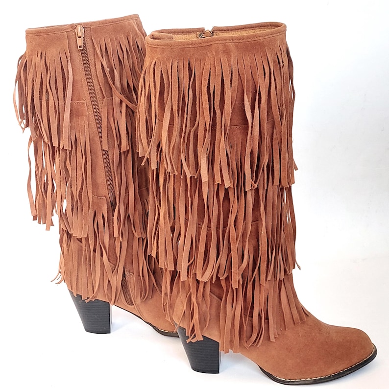 May include: A pair of brown suede boots with multiple layers of fringe. The boots have a zipper closure on the side and a small heel. The boots are approximately 30 cm tall.