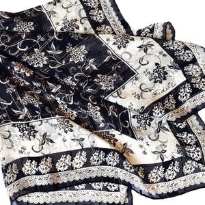 May include: A black and white silk scarf with a floral pattern and lace trim. The scarf features a repeating design of flowers and leaves, with a contrasting border. The scarf is folded and draped, showcasing its intricate details and elegant design.