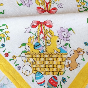 May include: White Easter-themed fabric with a repeating pattern of yellow bunnies, Easter eggs, flowers, and a basket. The basket is filled with yellow bunnies and colorful eggs. The fabric has a yellow border.