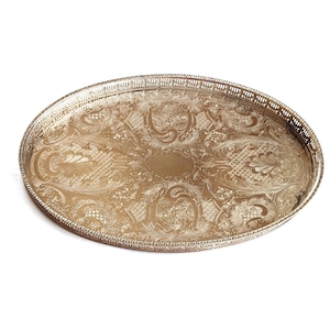Può includere: Un vassoio da portata ovale in metallo color argento con un intricato motivo floreale e a volute in rilievo su tutta la superficie. Il vassoio presenta un bordo rialzato e traforato con un delicato design a griglia lungo il perimetro.