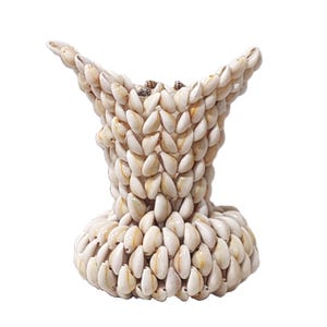 Puede incluir: Un jarrón decorativo hecho de numerosas conchas marinas pequeñas de color crema. El jarrón tiene una parte superior acampanada y una base redondeada, con las conchas meticulosamente dispuestas para crear una superficie texturizada. La forma general recuerda a un cáliz.