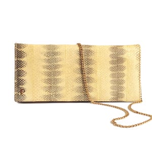 May include: A cream and grey snakeskin-patterned clutch bag with a gold chain strap. The rectangular bag features a small gold logo and is designed to be carried over the shoulder or as a clutch. The bag's dimensions are not visible.
