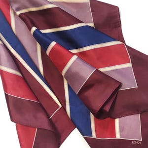 Peut inclure: Un foulard en soie avec un motif géométrique dans les tons de rouge, bleu, violet et crème. Le foulard est plié, mettant en valeur les blocs de couleurs et l'étiquette de la marque "ECHO".