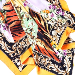 May include: A collection of silk scarves with vibrant patterns. The scarves feature a mix of floral, tiger stripe, and baroque designs. Colors include orange, black, gold, and purple. The word "CODELLO" is visible on one scarf.