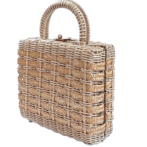 May include: A woven handbag with a rectangular shape and a curved handle. The bag is made of light brown wicker material, with a grid-like pattern. It has a clasp closure and a structured design, suitable for carrying essentials.