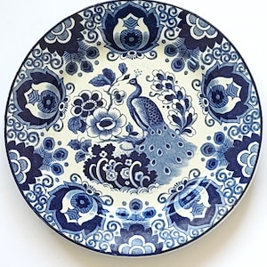 May include: A blue and white ceramic plate featuring a peacock design. The plate depicts a peacock with its tail feathers spread, surrounded by floral patterns. The plate has a white background with blue and white floral designs.