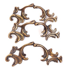 May include: Three ornate gold-toned metal cabinet pulls with a decorative scroll design.