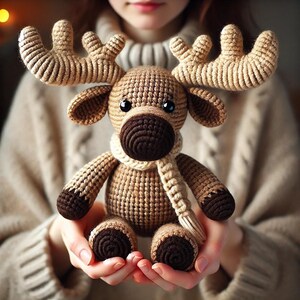 Op de afbeelding: Een gehaakt rendier speelgoed van bruin en wit garen, met een witte sjaal. Het rendier heeft een bruine neus en grote, blauwe ogen.