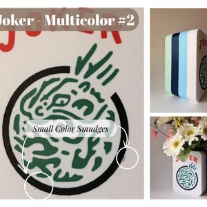 May include: A white rectangular vase with rounded corners featuring the text Joker - Multicolor #2 and a circular green abstract graphic. The side panels display vertical stripes in light green, dark blue, and light blue. Small color smudges are visible.
