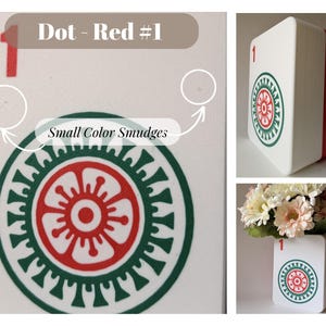 May include: A white rectangular container with a red side, featuring a red number 1 and a circular green and red floral-style graphic. The surface shows small color smudges. The object is shown from multiple angles, including one with flowers.