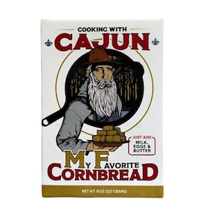 May include: A box of Cajun-style cornbread mix featuring a cartoon illustration of a man with a beard and a hat. The box says "Cooking with Cajun" and "My Favorite Cornbread".