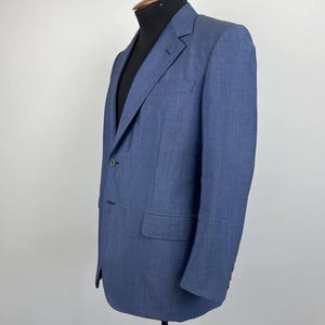 May include: A blue blazer with a two-button fastening, notched lapels, and a single chest pocket. The jacket is displayed on a mannequin. The blazer has a classic, tailored fit and is made of a textured fabric.