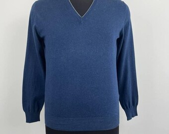Könnte beinhalten: Ein marineblauer V-Ausschnitt-Pullover mit langen Ärmeln. Der Pullover hat einen weißen Besatz um den Halsausschnitt und wird auf einer Schaufensterpuppe präsentiert. Der Pullover ist aus einem weichen Material gefertigt und hat gerippte Bündchen und Saum.