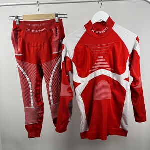 May include: Red and white athletic base layer set. The set includes a long-sleeved shirt and leggings. The shirt has white accents and the text "X BIONIC" on the collar. The leggings also have the text "X BIONIC".