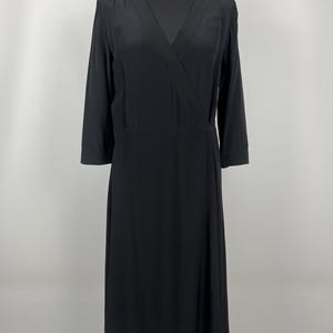 May include: A solid black midi-length dress featuring a V-neckline, a wrap-style bodice, and three-quarter length sleeves. The garment has a straight waist seam and a skirt that falls to a mid-calf length, providing a simple and clean silhouette.