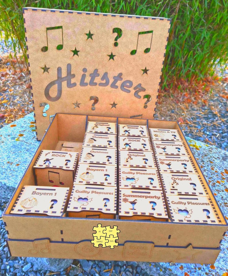 K&ouml;nnte beinhalten: Eine braune Holzspielbox mit dem ausgeschnittenen Wort "Hitster". Im Inneren befinden sich kleinere Boxen mit Aufschriften wie "Rock" und "Summerparty". Das Design umfasst Noten, Sterne und Fragezeichen, die in das Holz geschnitten sind.