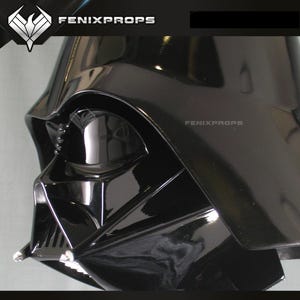 May include: A glossy black Darth Vader helmet, a Star Wars character, with the FENIXPROPS logo visible. The helmet's design includes a distinctive face mask and a prominent brow. The image is a close-up, highlighting the helmet's details.