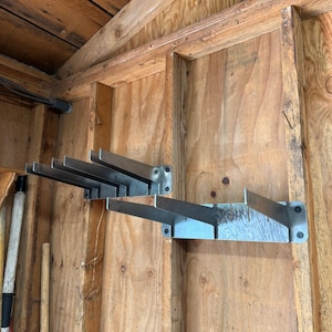 Puede incluir: Dos estanterías metálicas de pared con múltiples ranuras anguladas, fijadas a una pared de madera. Las estanterías son de metal color plata y están diseñadas para guardar objetos. La pared de madera tiene vetas naturales.