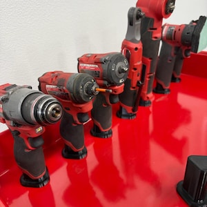 May include: Several red and black power tools, such as drills and sanders, are displayed on a shiny red surface. The tools vary in size and design, indicating different uses. The lighting is good, showing the tools' features clearly.