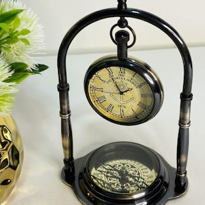 May include: A vintage clock and compass set with a black and bronze finish. The clock, marked "VICTORIA LONDON 1876," hangs above a compass. The words "Rustic Charm" are in the upper right corner.