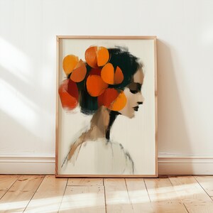 Könnte beinhalten: Abstrakter Kunstdruck einer Frau im Profil, mit dunklem Haar, das mit großen orangefarbenen Formen geschmückt ist. Das Kunstwerk ist in hellem Holz gerahmt und vor einem neutralen Hintergrund platziert, was einen auffälligen visuellen Kontrast erzeugt. Die Farbpalette umfasst Orange-, Schwarz- und Beigetöne.