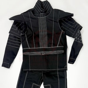 May include: Black costume with white stitching. The outfit has a high collar, shoulder pads, and long sleeves. The design includes vertical lines down the front and geometric patterns on the sleeves. The costume appears to be made of a smooth, possibly synthetic fabric.