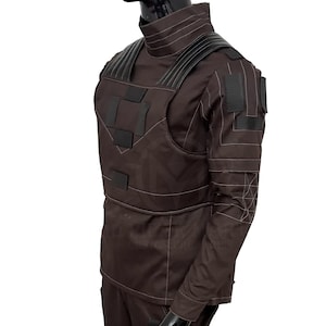 Puede incluir: Uniforme t&aacute;ctico marr&oacute;n con detalles negros. El atuendo presenta un cuello alto, hombros acolchados y m&uacute;ltiples parches rectangulares. Las costuras blancas delinean el dise&ntilde;o, creando una apariencia estructurada. El uniforme est&aacute; dise&ntilde;ado para protecci&oacute;n y funcionalidad.