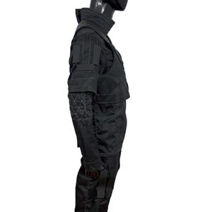 Puede incluir: Traje t&aacute;ctico negro con cuello alto, m&uacute;ltiples bolsillos y paneles reforzados. El traje incluye una chaqueta y pantalones, con costuras geom&eacute;tricas en las mangas. El dise&ntilde;o sugiere una est&eacute;tica futurista o militar.