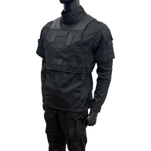 Puede incluir: Chaleco t&aacute;ctico negro con m&uacute;ltiples bolsillos y cuello alto. El chaleco se lleva sobre una camisa negra de manga larga y pantalones negros. El maniqu&iacute; lleva guantes negros.