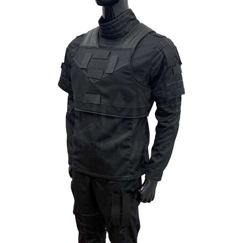 Puede incluir: Chaleco t&aacute;ctico negro con m&uacute;ltiples bolsillos y cuello alto. El chaleco se lleva sobre una camisa negra de manga larga y pantalones negros. El maniqu&iacute; lleva guantes negros.