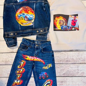 K&ouml;nnte beinhalten: Ein Kinderbekleidungsset mit Jeansjacke, Jeans und Kapuzenpullover mit Hot Wheels-Grafiken. Die Jacke und Jeans tragen den Namen "Jamari" und Hot Wheels-Logos. Der Hoodie hat ein Foto und Hot Wheels-Grafiken. Die Jeans hat die Nummer "6".
