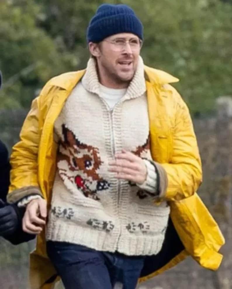 May include: A person wearing a navy blue beanie, glasses, and a yellow raincoat. They are also wearing a cream-colored zip-up sweater with a brown dog design. The sweater has Japanese characters at the bottom.