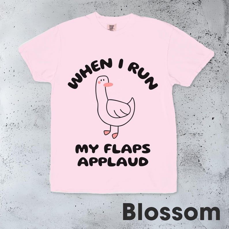 以下が含まれることがあります： ピンクのTシャツに、漫画のガチョウと「When I run my flaps applaud」というテキストが書かれています。