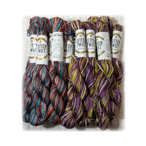 May include: Bundles of Cotton Twist yarn in various colors. The yarn is wrapped with labels that read "Cotton Twist". The yarn colors include teal, red, purple, and yellow. Ideal for knitting and crochet projects.
