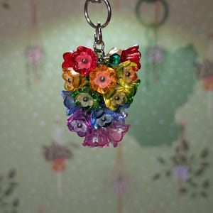 May include: A colorful keychain featuring a bouquet of translucent flowers in a rainbow of colors, including red, orange, yellow, green, blue, and purple. The flowers are attached to a silver-colored metal clasp.