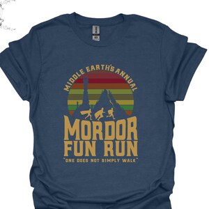 May include: A navy blue t-shirt with a vintage-style graphic of a mountain range with a sunset behind it. The text "Middle Earth's Annual Mordor Fun Run" is printed on the shirt, along with the quote "One does not simply walk."