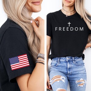 May include: Black t-shirts. One has the word "FREEDOM" with a cross above it. The other has an American flag patch on the sleeve. Both shirts are short-sleeved.