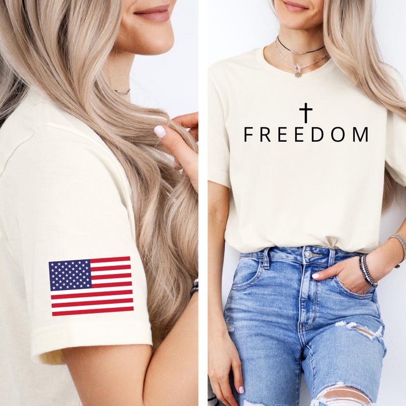 May include: Cream-coloured t-shirt with the word "FREEDOM" and a cross graphic. The left sleeve features a small American flag. The shirt is paired with blue jeans.
