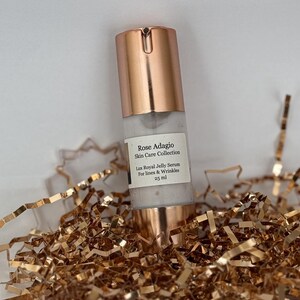 May include: A rose gold bottle of serum labelled "Rose Adagio Skin Care Collection Lux Royal Jelly Serum For lines & Wrinkles 25 ml".