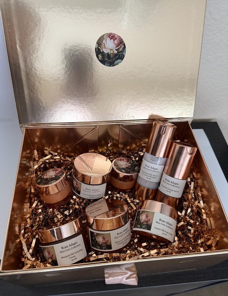 May include: A set of six rose-themed skincare products in a gold gift box. The products include a face cream, a serum, and a lotion. The box is filled with gold tissue paper.