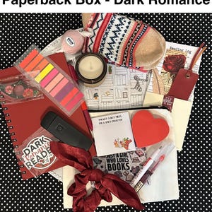 May include: A curated "Dark Romance" themed gift box with a red notebook, candle, socks, and other accessories. Includes a bookmark, sticky notes, and a scrunchie. The box is filled with items for book lovers.